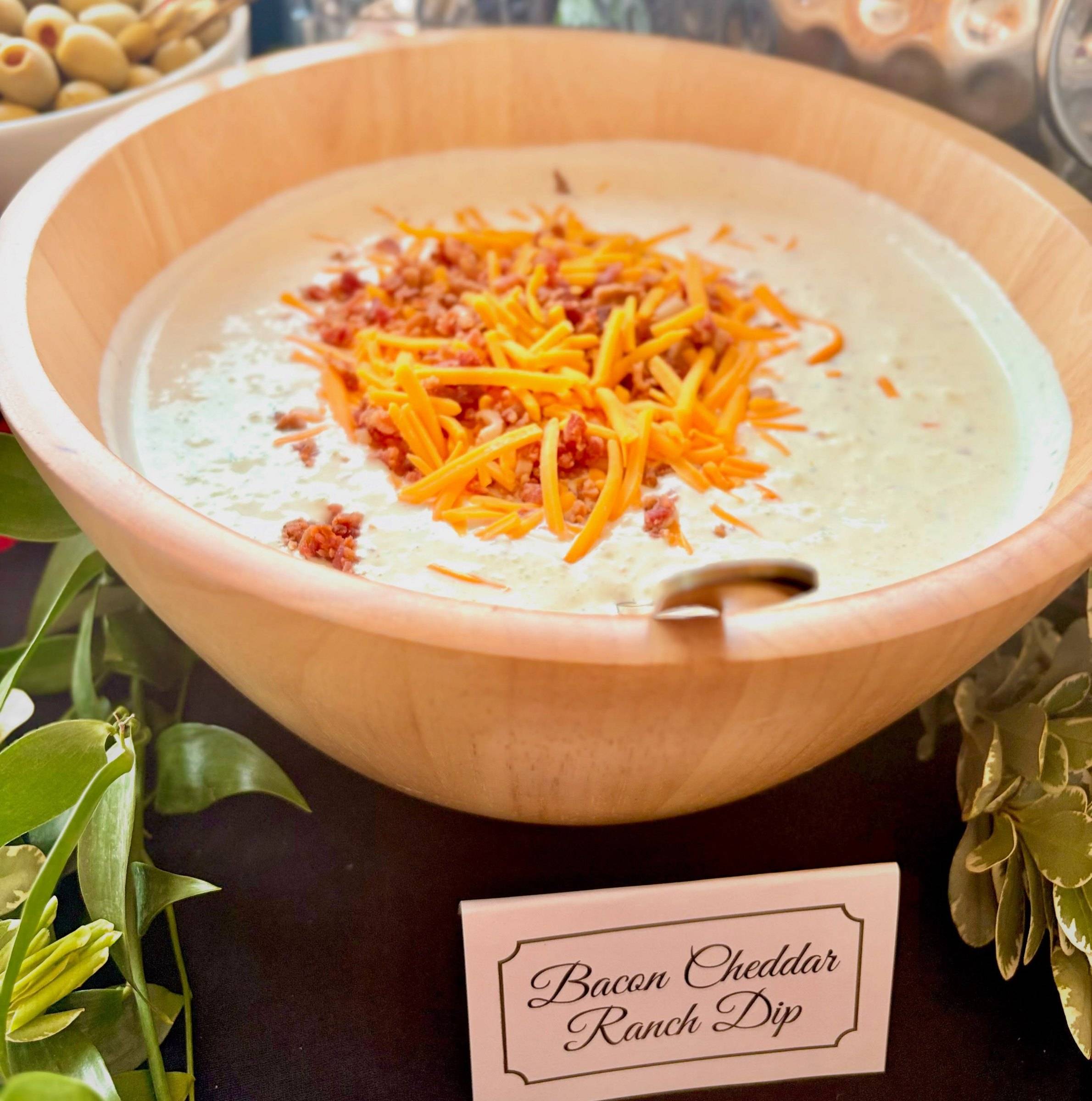 Bacon cheddar ranch dip topped with shredded cheddar and bacon in a wooden bowl